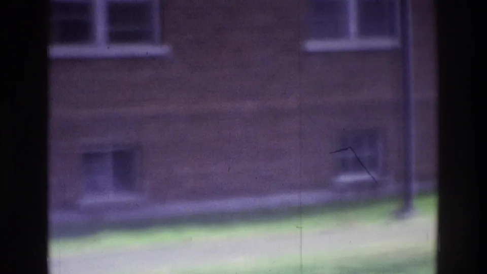 1975 Atlanta 8mm frame showing a soft, distant courtyard view with brick walls, white windows, grass, and a dark vertical film edge.
