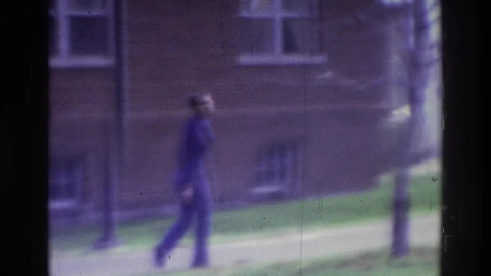 1975 Atlanta 8mm frame with an unidentifiable person near lampposts in front of a brick building and grassy courtyard.