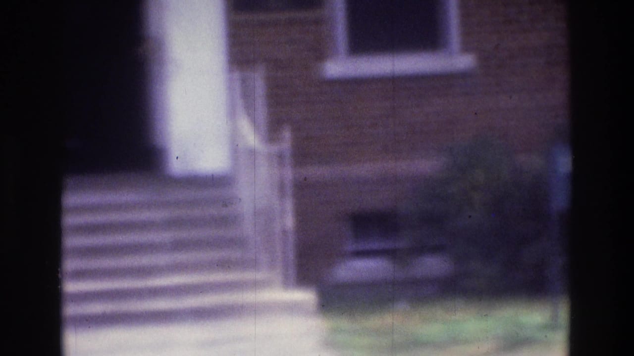 Brick building entrance with white column, steps, window, and lawn.