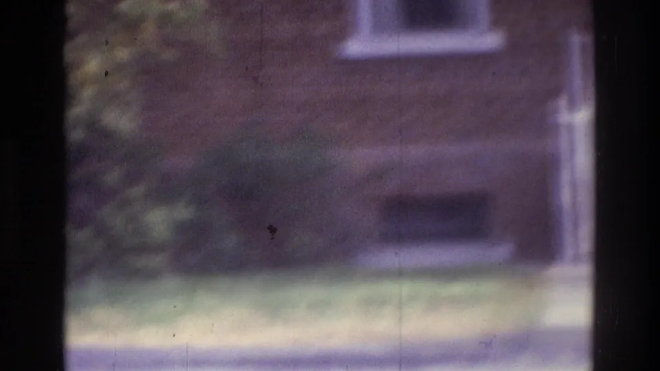 1975 Atlanta 8mm frame with a blurred brick facade, lower windows, grass, walkway, and shrubs near the building.