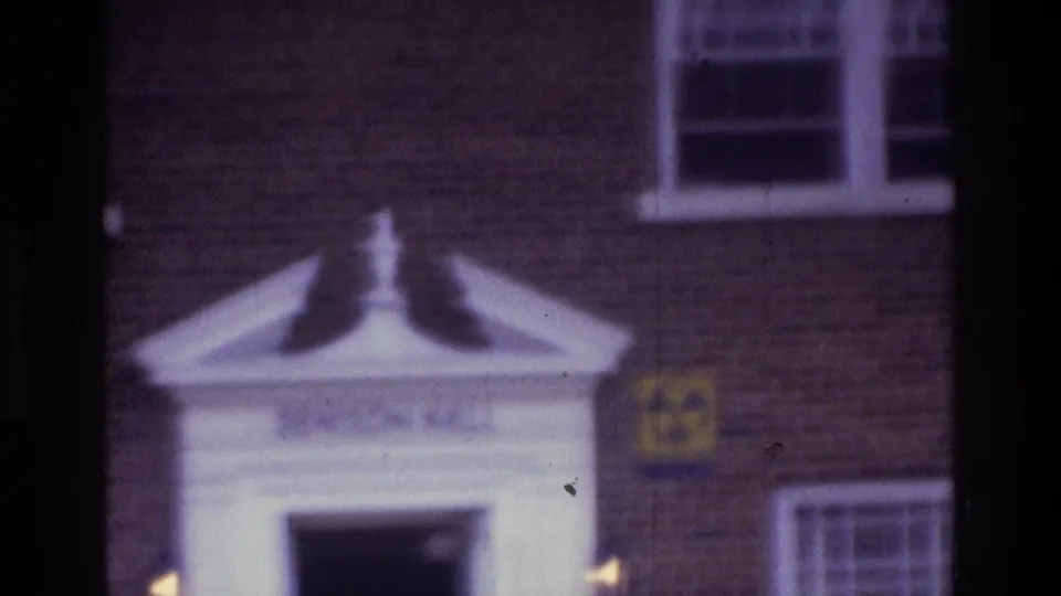 1975 Atlanta 8mm frame of a brick building facade with white entrance detail, windows, and a visible fallout-shelter sign.