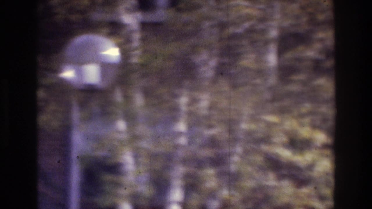 1975 Atlanta 8mm frame with a lamppost in front of trees and a brick exterior, rendered with heavy blur and color shift.