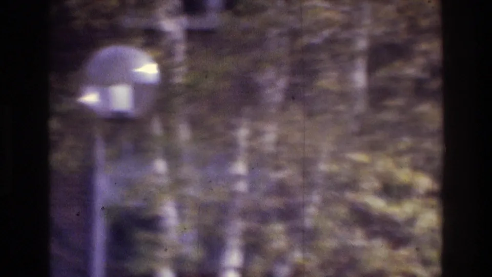 1975 Atlanta 8mm frame with a lamppost in front of trees and a brick exterior, rendered with heavy blur and color shift.
