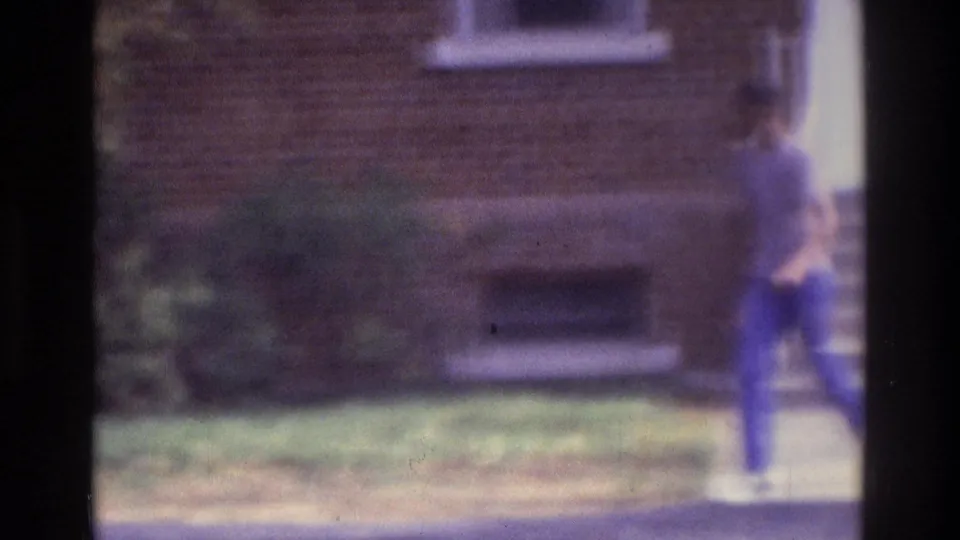 At the end of the 1975 Atlanta clip, the teenager moves across the frame near grass and the brick building facade.