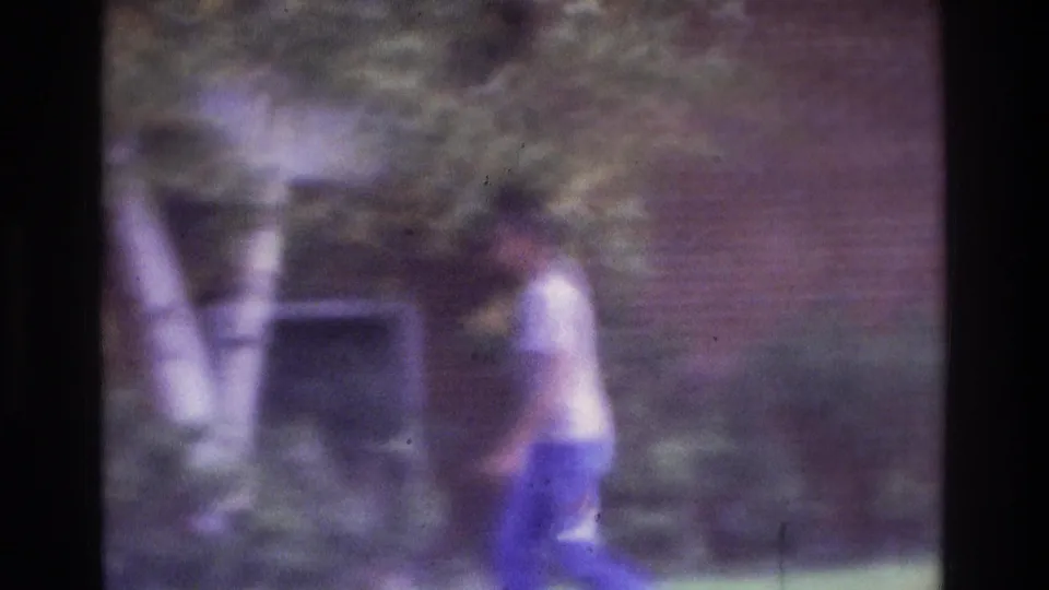 1975 Atlanta home-movie frame of a man walking across a grassy residential area near a brick building and trees.