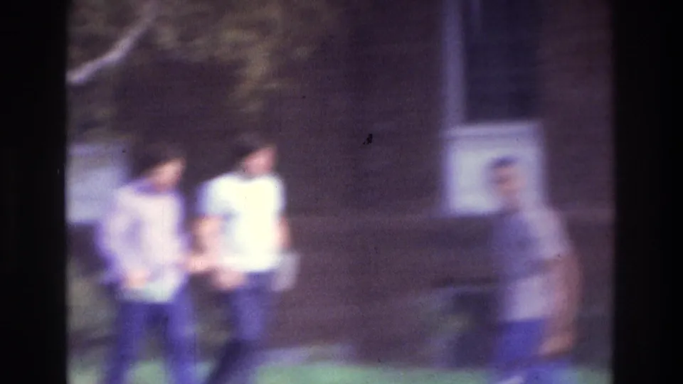 1975 Atlanta home-movie frame showing two people near a brick building, with another blurred figure at the edge of the scene.