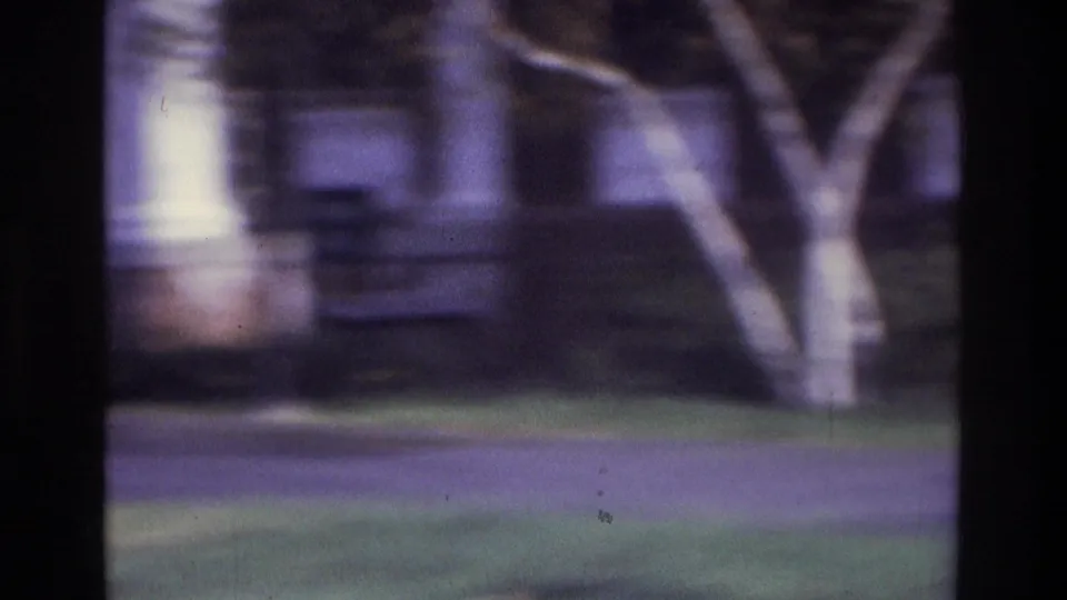 1975 Atlanta home-movie frame showing a brick residential building, tree trunk, lawn, and path with no clear person centered.