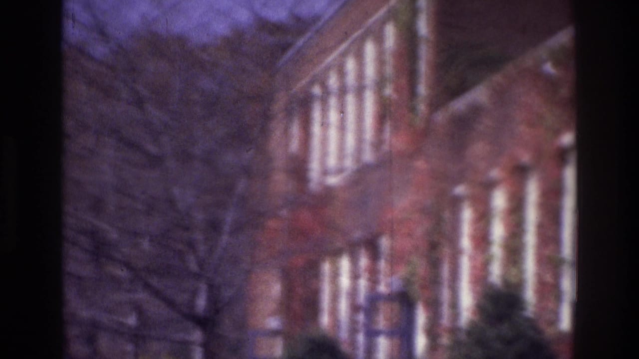1975 Atlanta 8mm frame showing a blurred scan past brick campus-like buildings, white window trim, and leafless branches.