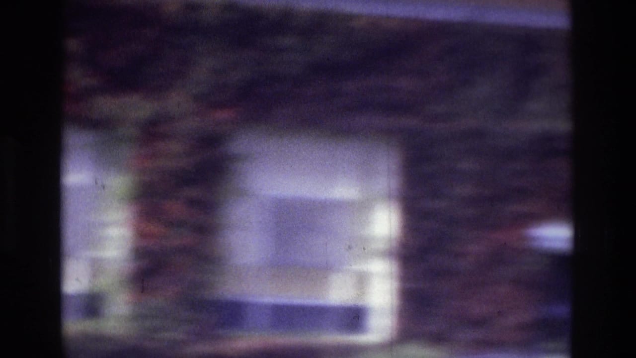 1975 Atlanta 8mm frame with a soft view of a brick exterior, white-framed window, and dark vertical film or scan edge.