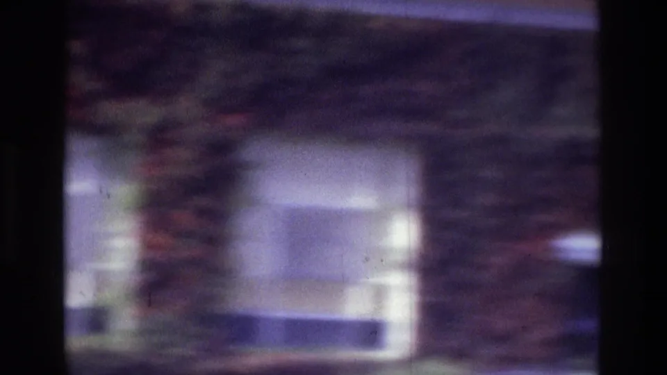1975 Atlanta 8mm frame with a soft view of a brick exterior, white-framed window, and dark vertical film or scan edge.