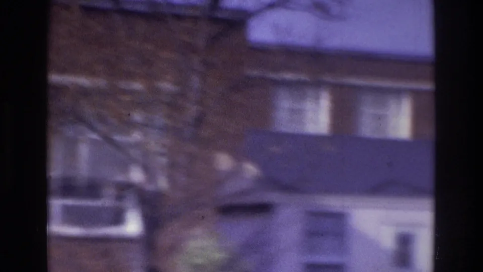 1975 Atlanta 8mm frame showing a passing view of rooflines, windows, bare trees, and washed pale sky.