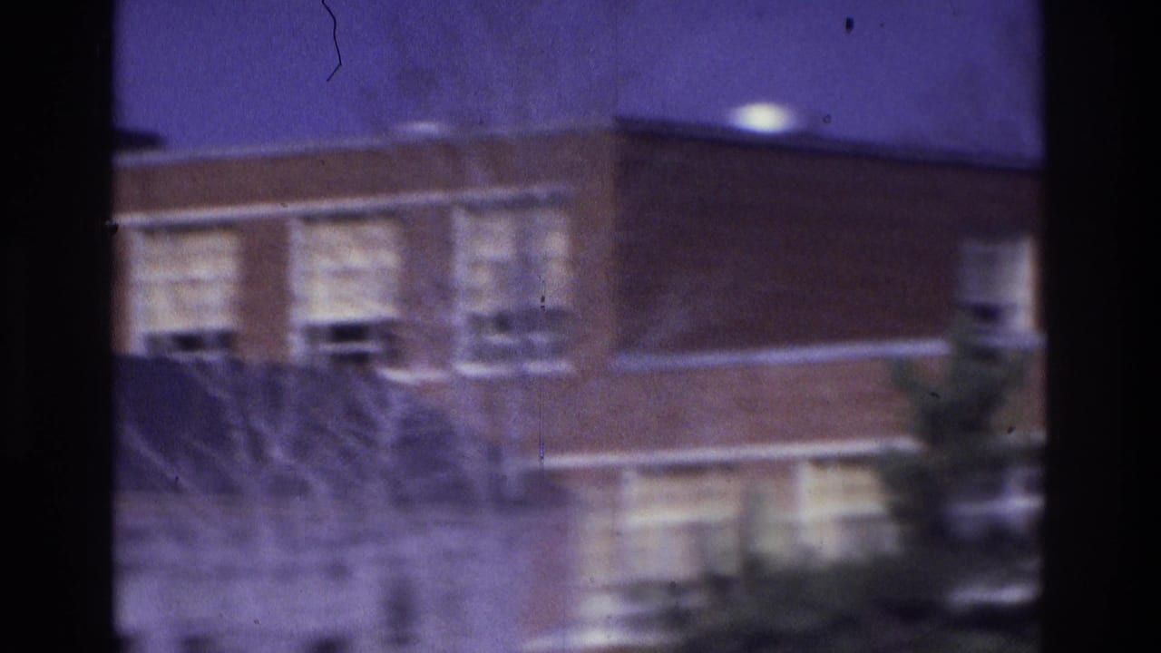 1975 Atlanta home-movie frame showing a soft distant brick building exterior with windows, trees, sky, and dark vertical framing.