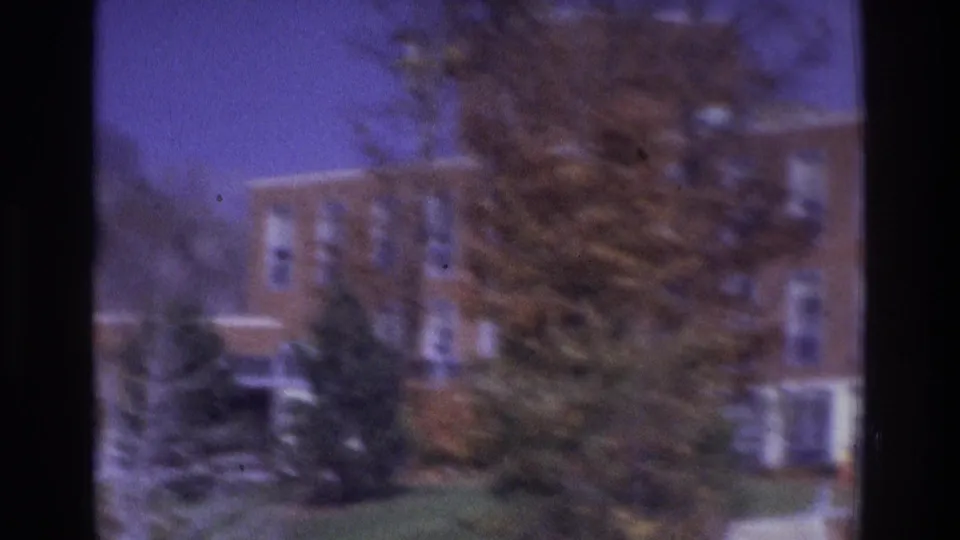 1975 Atlanta home-movie frame showing a brick building beyond grass and trees, with soft focus and purple-blue film color shift.