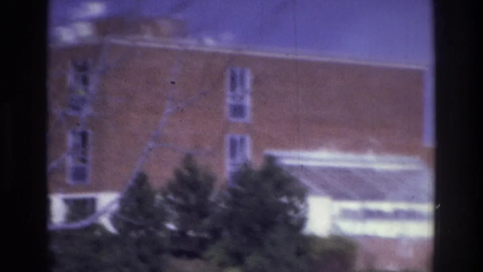 1975 Atlanta frame showing a brick building facade with vertical windows, trees, shrubs, and a bright foreground awning or structure.