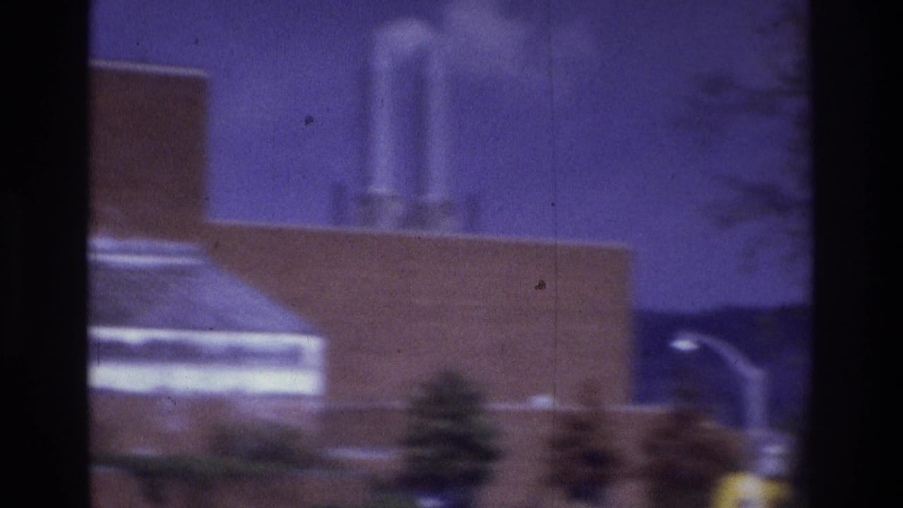 1975 Atlanta 8mm frame showing a blurred brick building, pale roof edge, smokestack-like forms, trees, and purple sky through dark vertical bars.