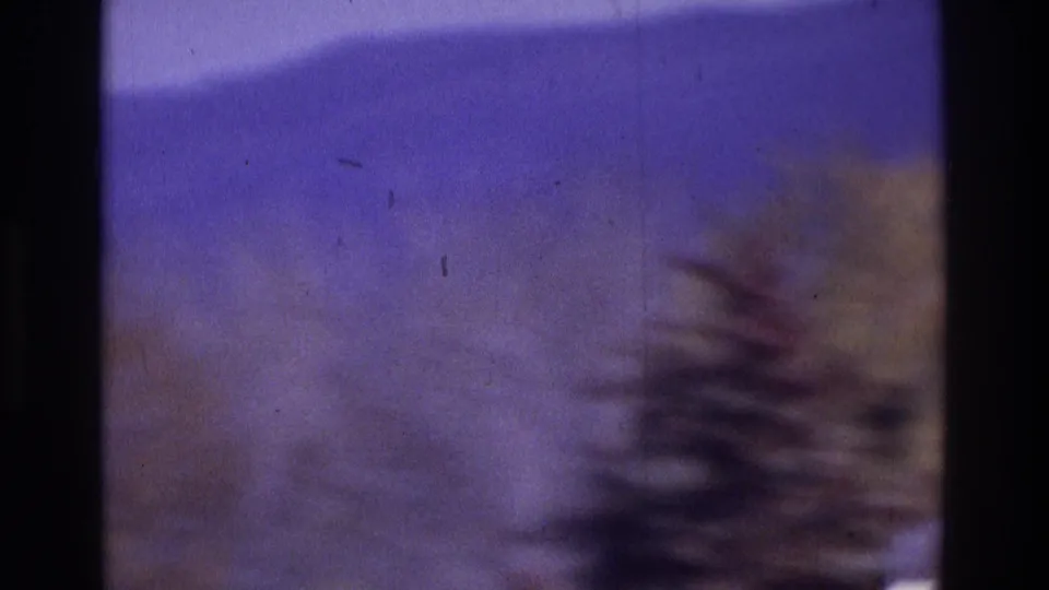 1975 Atlanta-area 8mm frame showing a motion-blurred wooded hill beneath a purple-tinted sky, with visible film edge and grain.