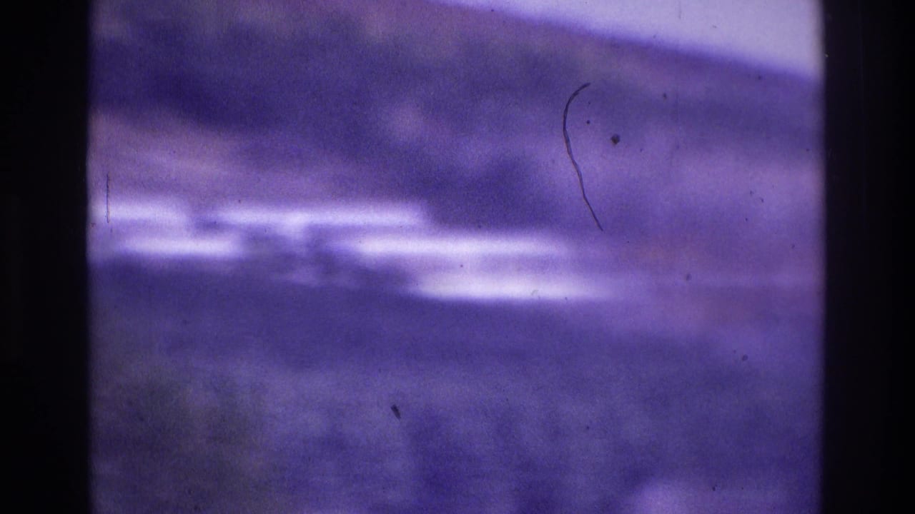 Soft-focus 1975 Atlanta home-movie frame showing an indistinct outdoor scene with purple color cast and dark film-edge borders.