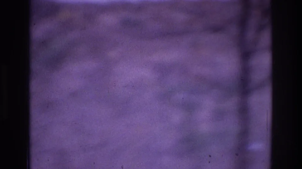 Soft, purple-tinted 1975 8mm frame from the Atlanta metadata set, showing blurred hills or water through dark foreground bands.