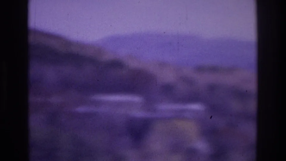 Purple-tinted 8mm home-movie frame showing a soft view of water and distant hills through dark foreground bars, based on the supplied Atlanta 1975 metadata.