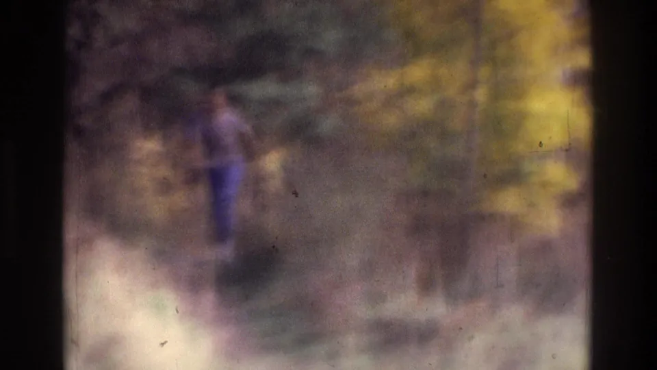 A distant figure in a purple shirt walks through woods in the 1975 Atlanta home-movie clip, softened by motion blur and film grain.