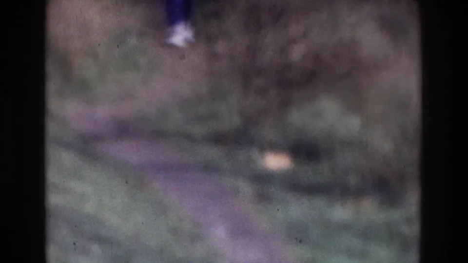 A soft-focus 1975 Atlanta frame shows an adult's lower body moving through a grassy wooded trail area.