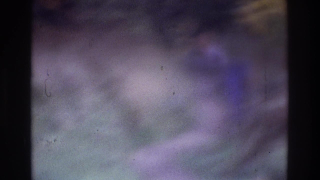 Blurry 1975 Atlanta home-movie frame showing a barely resolved person outdoors amid foliage and strong film wear.