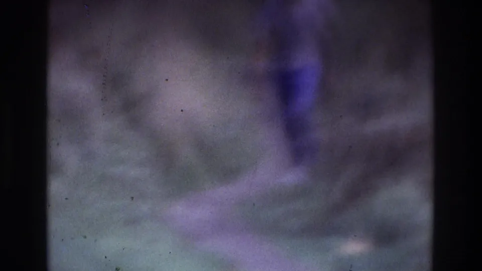 1975 Atlanta 8mm frame of an adult figure walking outdoors, heavily softened by motion blur, grain, and aged film marks.