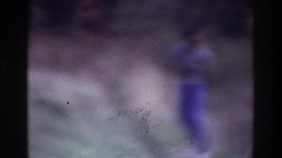 Soft 1975 Atlanta home-movie frame with a blurred adult figure at right walking through an outdoor natural setting.