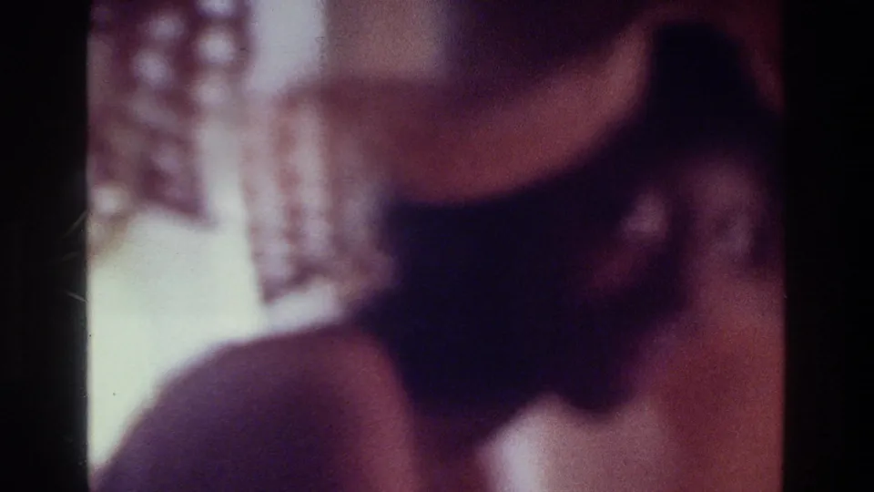 1975 Bronx 8mm close view of a woman beneath a wide straw hat, with curtain detail and warm interior color.