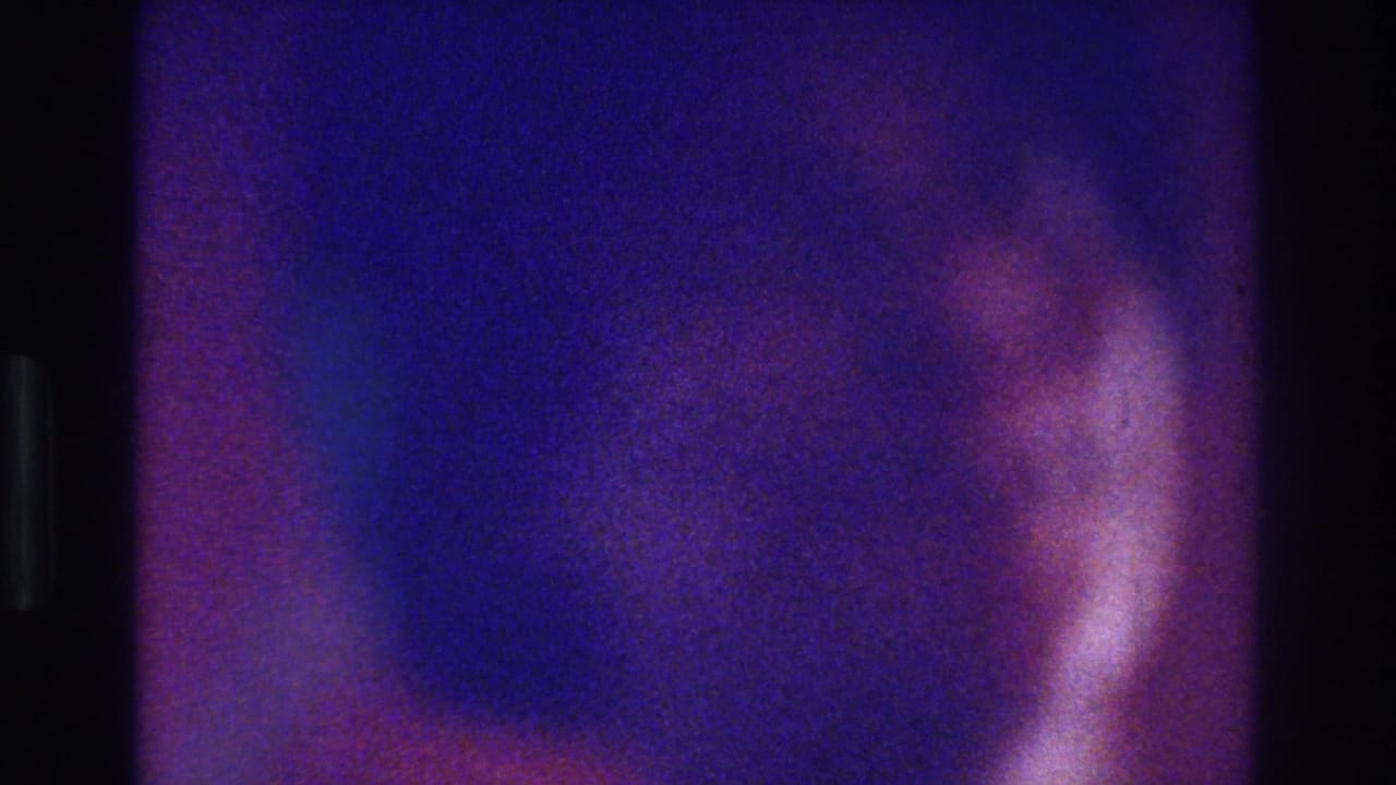 1975 Bronx home-movie frame with purple-blue fading and a soft silhouetted figure near a bright interior light source.