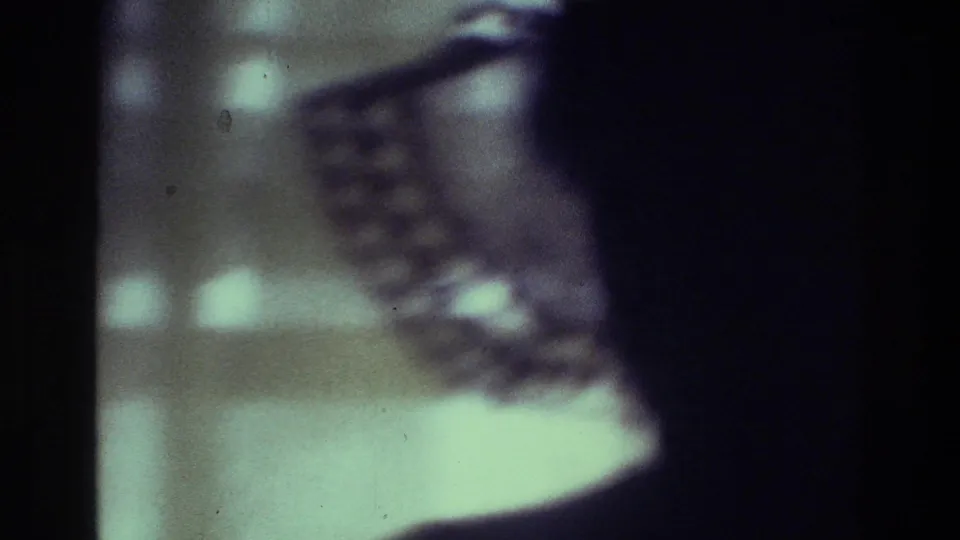 1975 Bronx 8mm frame with a dark side silhouette and blurred patterned hat or head covering against a bright interior background.