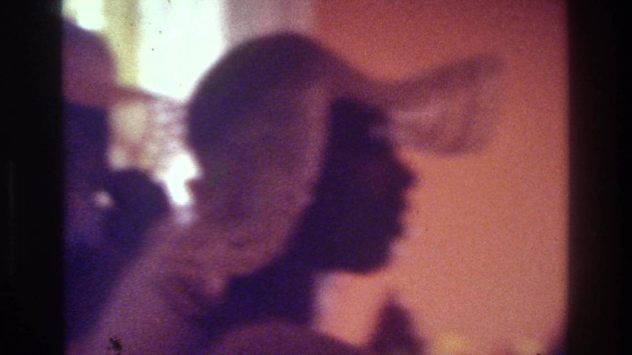 Silhouetted woman in a patterned hat faces right against a warm interior wall.