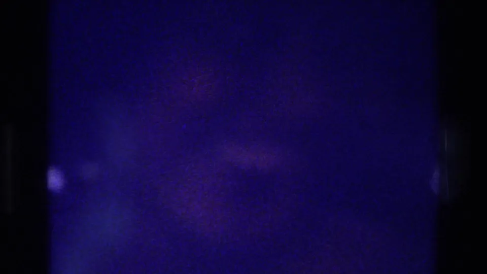 Mostly abstract 8mm frame from the 1975 Bronx clip, showing blue-purple density, grain, and a small bright mark near the left side.