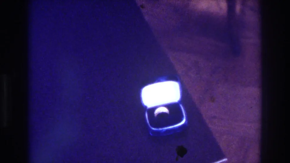 1975 Bronx 8mm frame showing a small open ring box on a dark surface, with strong blue-purple color shift and visible grain.