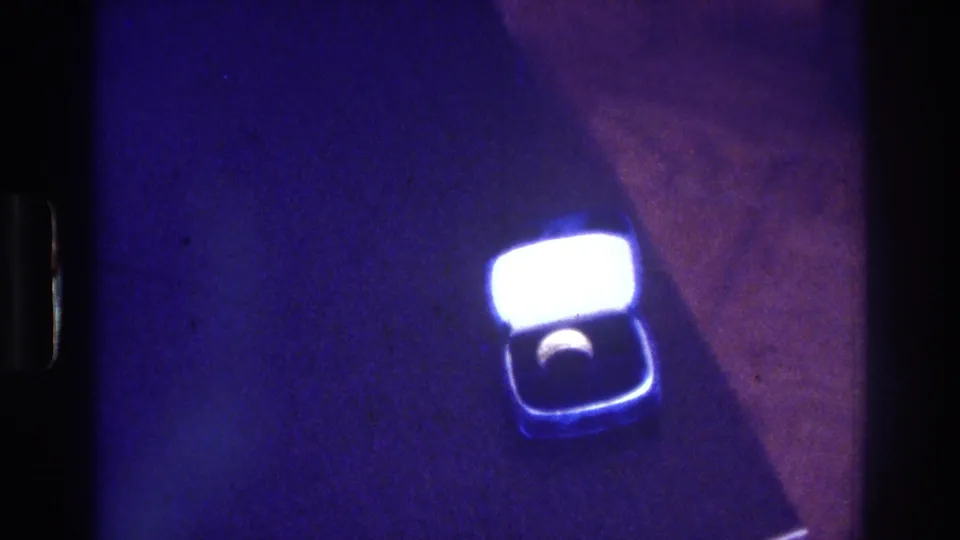1975 Bronx 8mm frame with a small open ring box viewed from above, its lid glowing brightly while the ring sits in shadow inside the box.