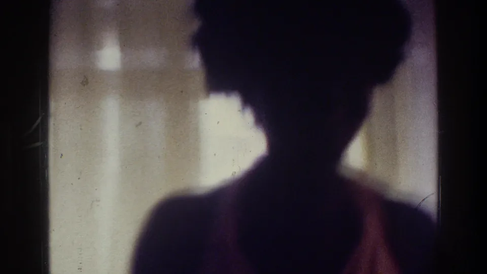 Tight 1975 Bronx frame of a woman's upper-body silhouette in a swimsuit, backlit by pale interior curtains.