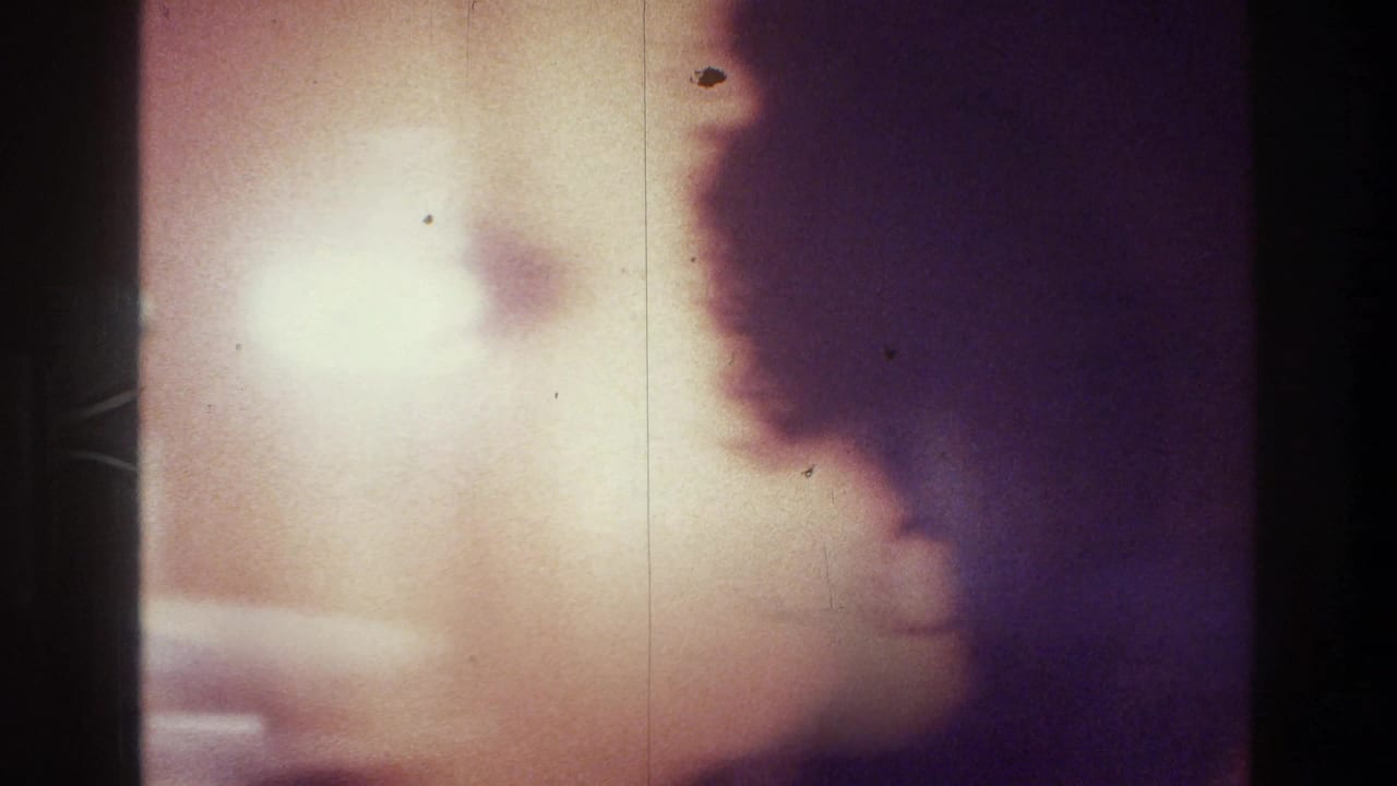 1975 Bronx 8mm frame showing a dark-haired woman in soft profile against a reddish wall, with heavy grain and low-light exposure.