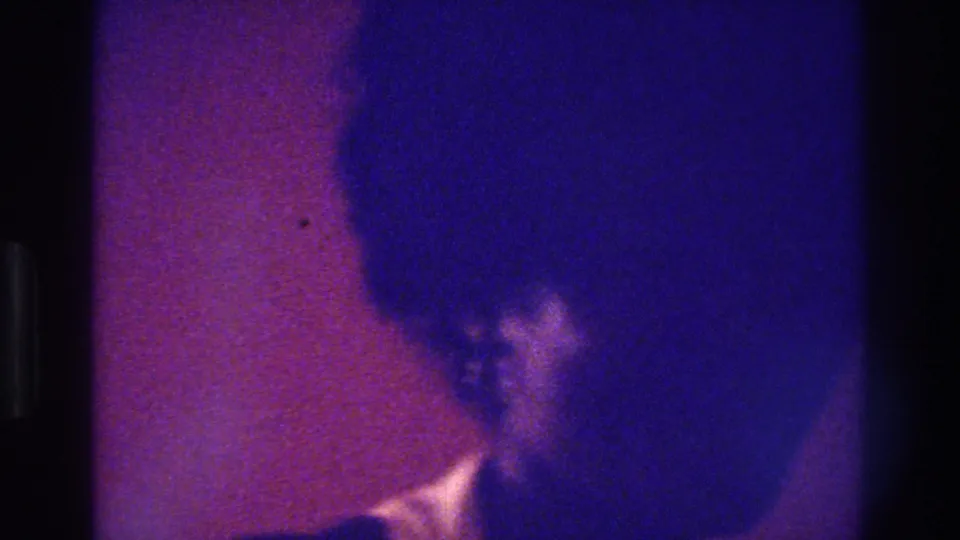 Low-light 1975 Bronx 8mm frame with a woman partly visible in blue-purple shadow near the right edge.