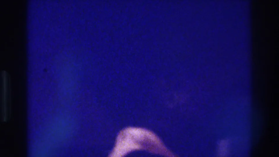 Underexposed 8mm frame from the Bronx night-out clip, showing blue grain and a soft pale shape near the lower edge.