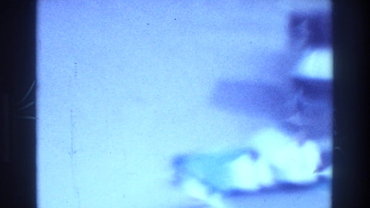 1975 Bronx 8mm frame with heavy blue cast, dark film borders, and soft indistinct forms that may show a waterfront or beach area.