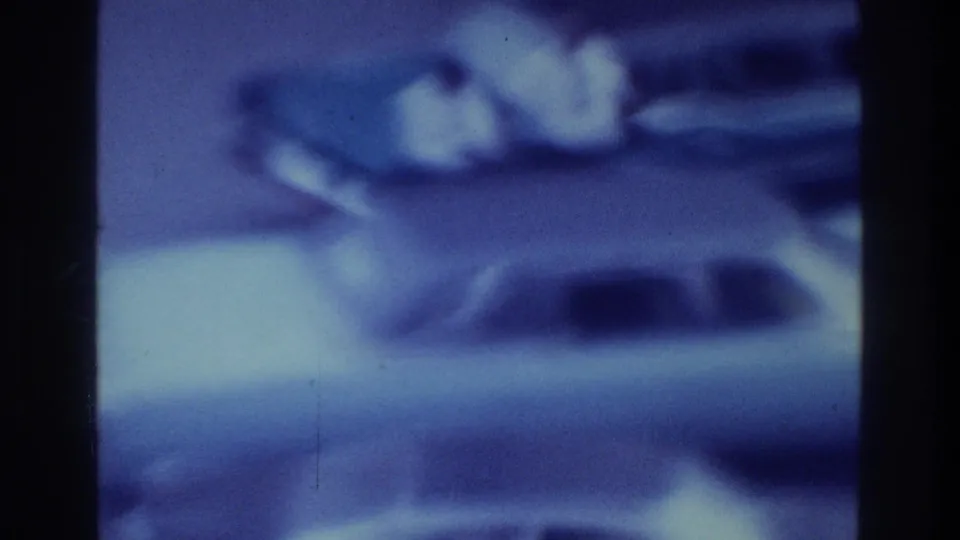 1975 Bronx 8mm frame with soft blue exposure, dark film borders, indistinct shoreline forms, and a low blurred foreground area.