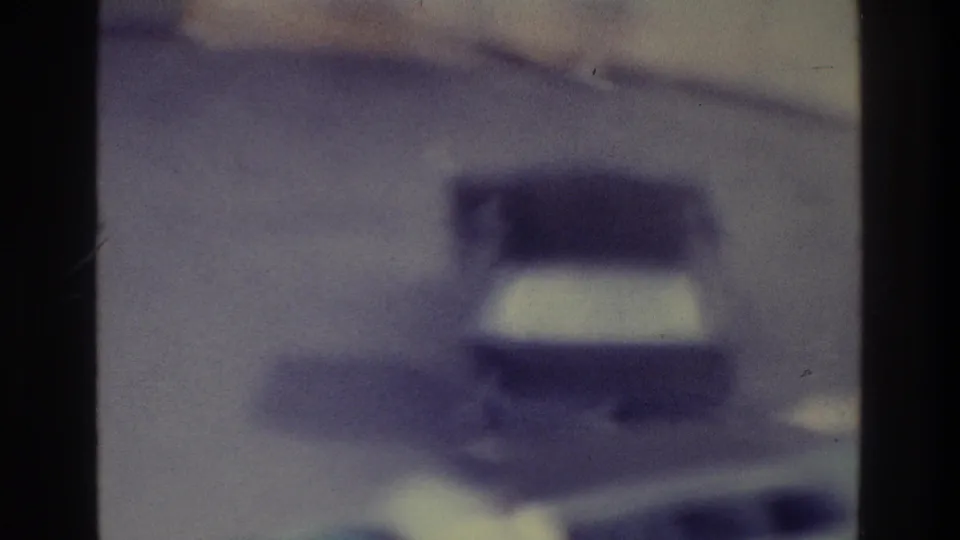 A 1975 Bronx road view shows an indistinct vehicle shape through soft focus, grain, and strong blue-purple color shift.