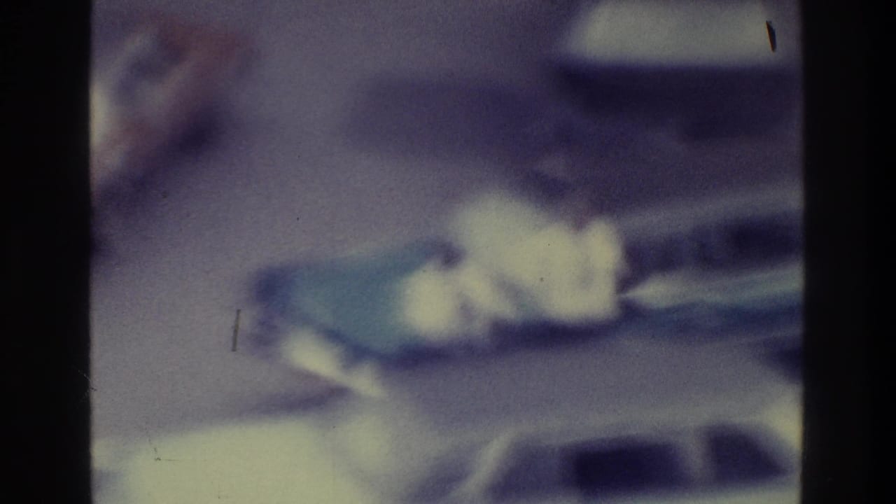 Soft, purple-tinted 1975 Bronx 8mm frame showing parked cars in a lot or street area, with no people clearly visible.