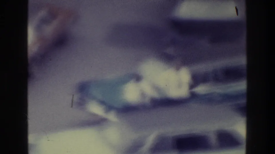Soft, purple-tinted 1975 Bronx 8mm frame showing parked cars in a lot or street area, with no people clearly visible.