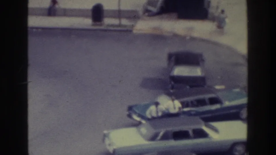 1975 Bronx frame with a dark station wagon partly beside a light sedan, a parked car ahead, and pedestrians along the sidewalk.