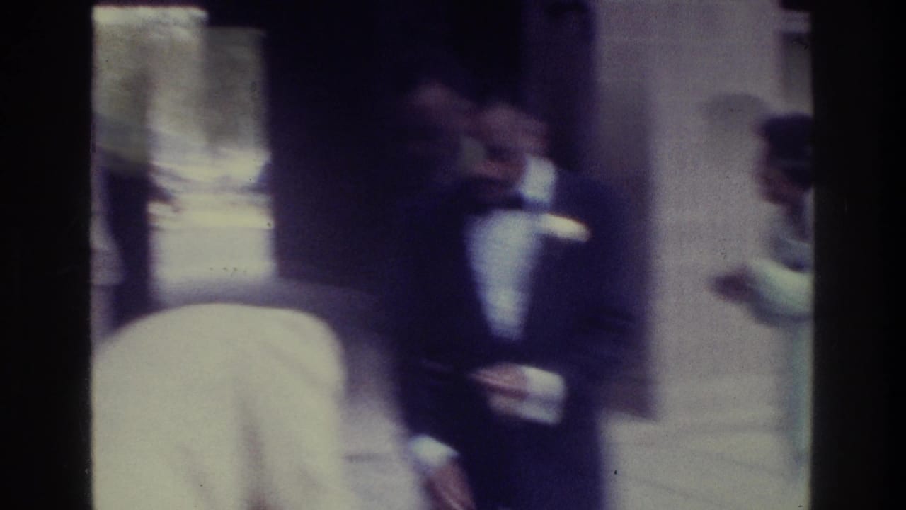 Formal guests stand near a doorway, including a man in a dark suit.