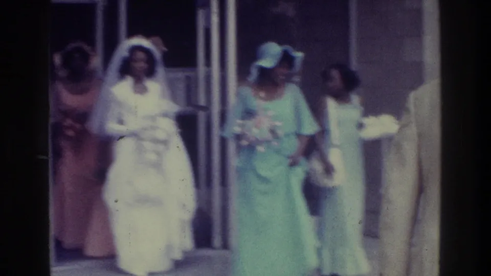 1975 Bronx wedding frame showing a bride in a white gown and veil leaving with women in pastel formal dresses.