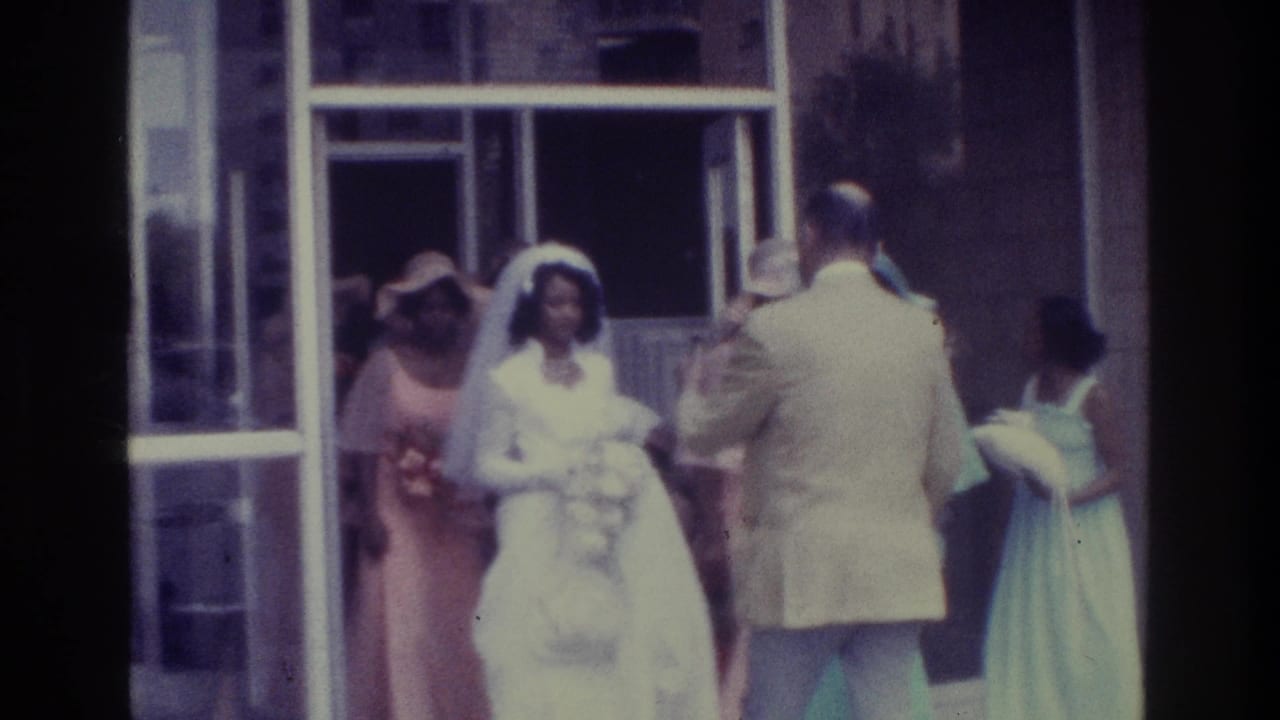 Bride and attendants stand near a chapel doorway as a man in a light suit faces them.