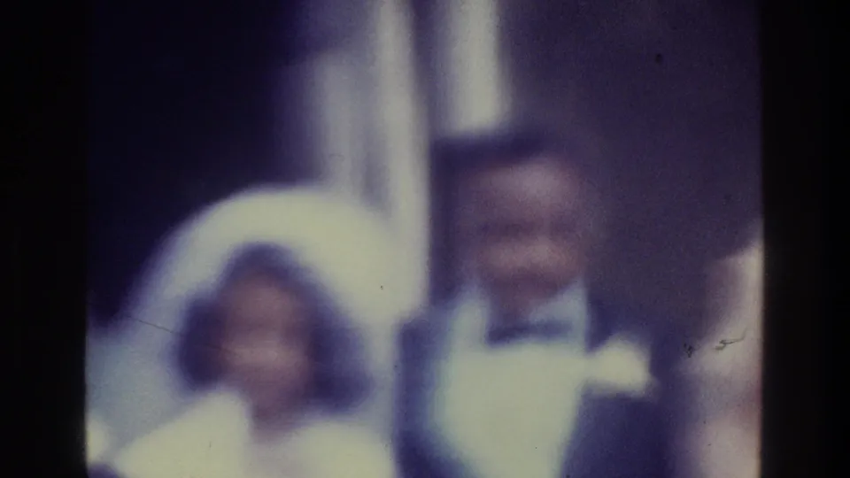 1975 Bronx wedding frame showing the bride and groom indoors, with another adult partly visible at the right edge.