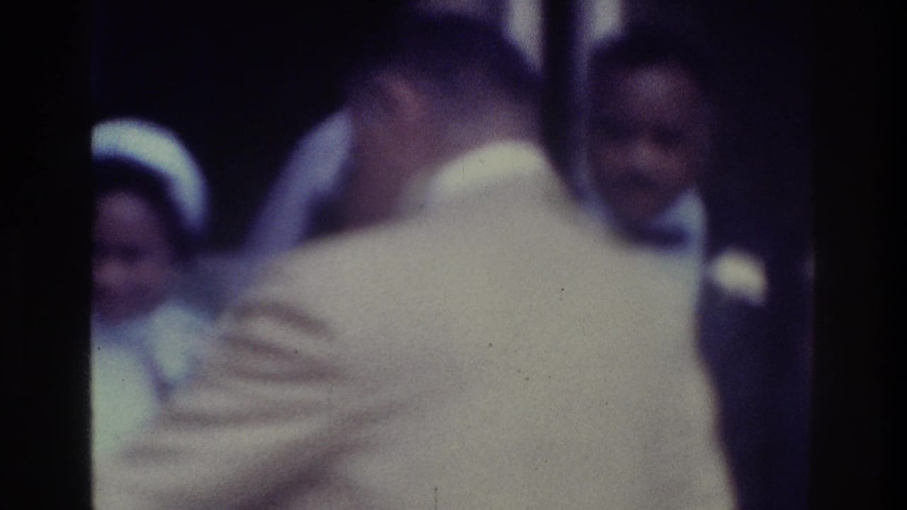 Man in a light jacket faces away near wedding guests and the groom.